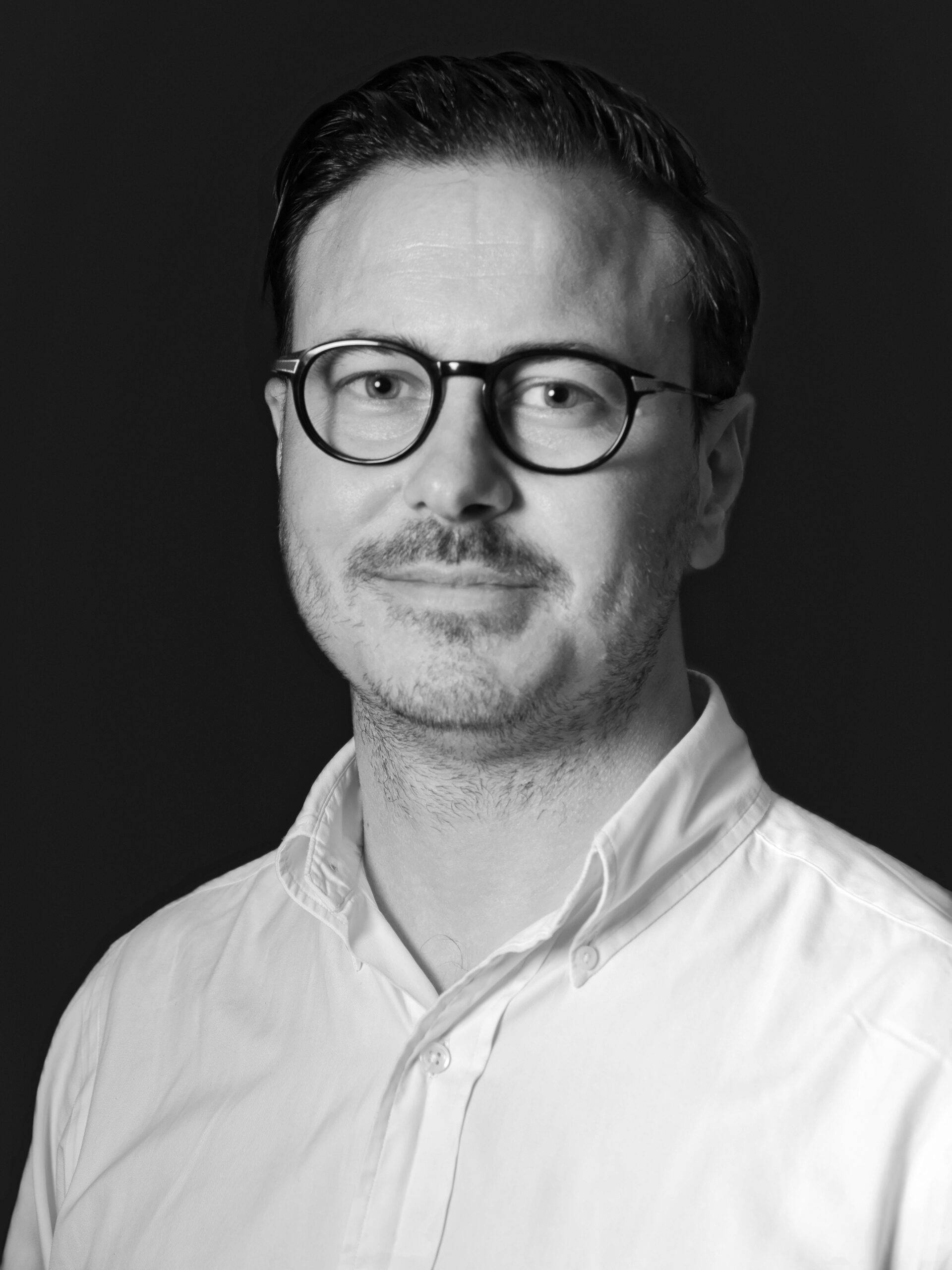 A black and white photo of a man wearing glasses posing for a headshot