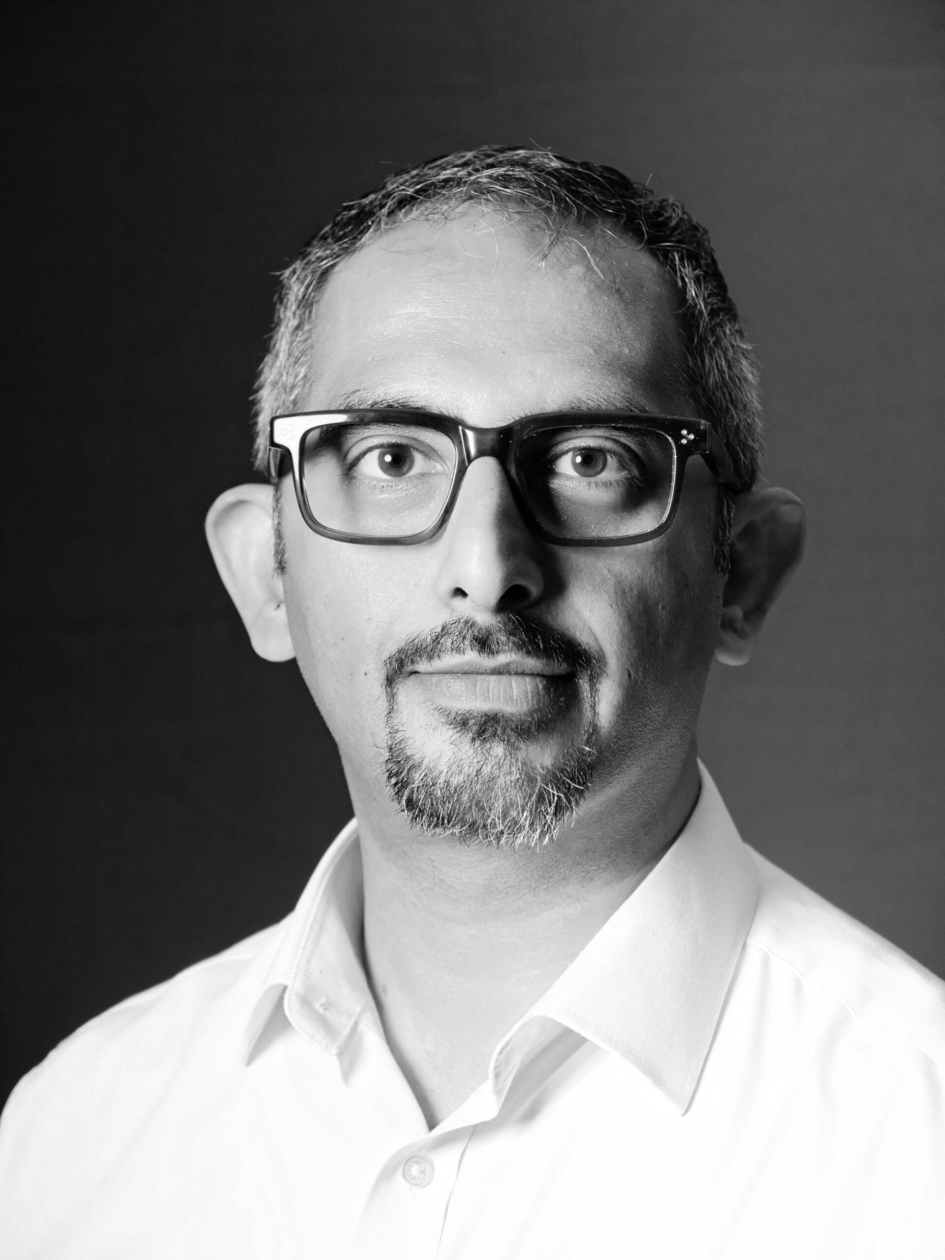 A black and white photo of a man wearing glasses posing for a headshot